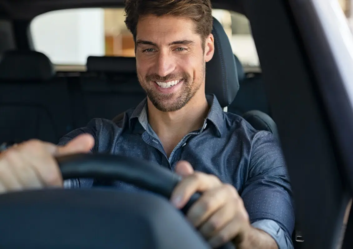 young man in blue shirt sitting behind wheel of car smiling