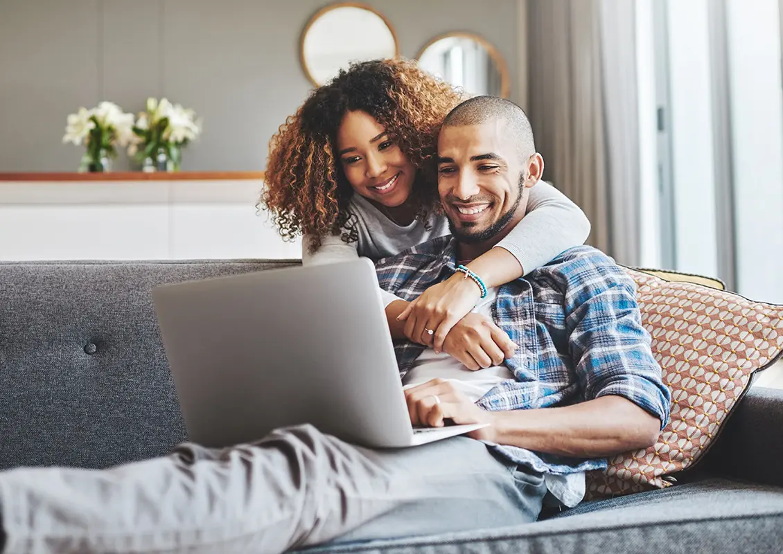 Man and woman sitting on a couch smiling at a laptop