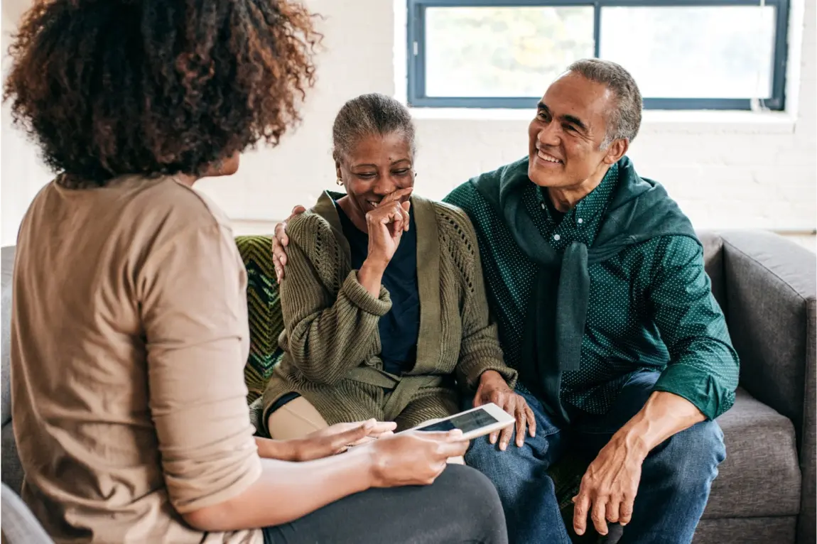 Older couple sitting on couch meeting with female financial advisor to discuss financial opportunities