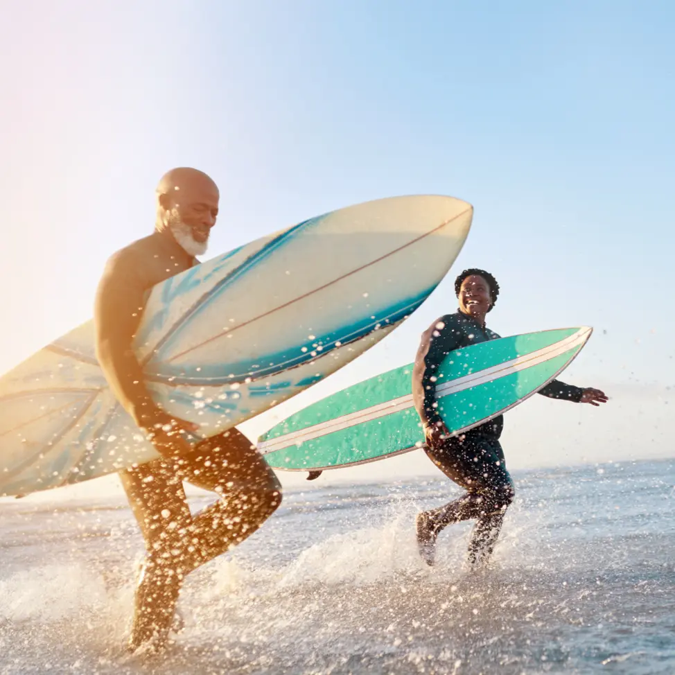 Two men with surfboards walking in the water and laughing