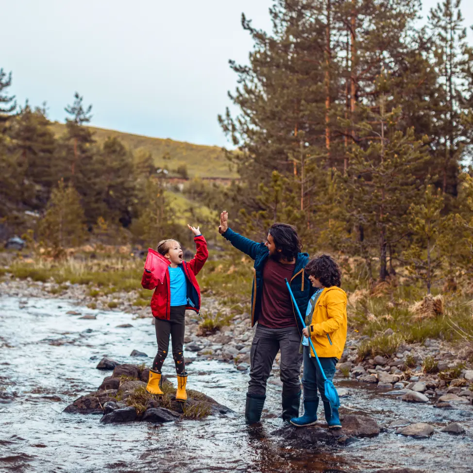 Father, daughter and son high-fiving in a stream in the woods